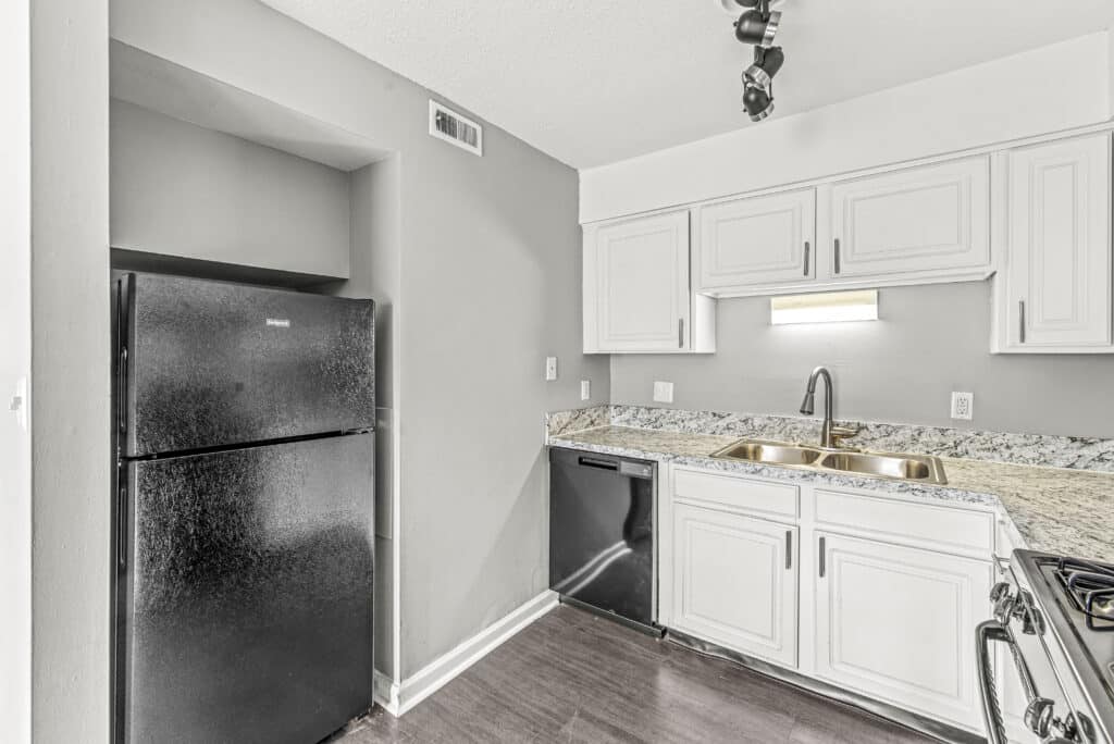 Modern kitchen with white cabinets, marble countertops, black refrigerator, black dishwasher, stainless steel sink, and gray walls.