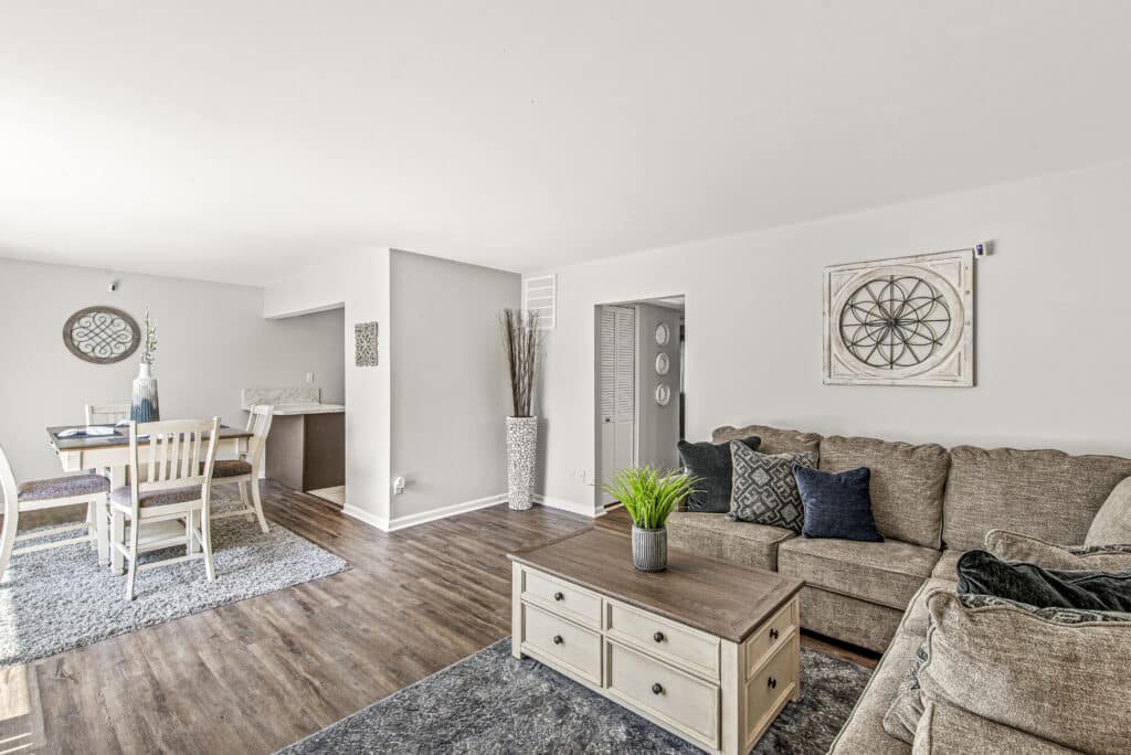 Bright living and dining area with beige sofas, wooden coffee table, dining set, wall art, and hardwood floors in a neutral-toned open layout.