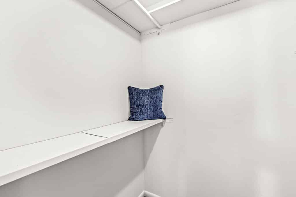 A single blue textured pillow sits on a white shelf against the plain white walls of an empty room or closet.