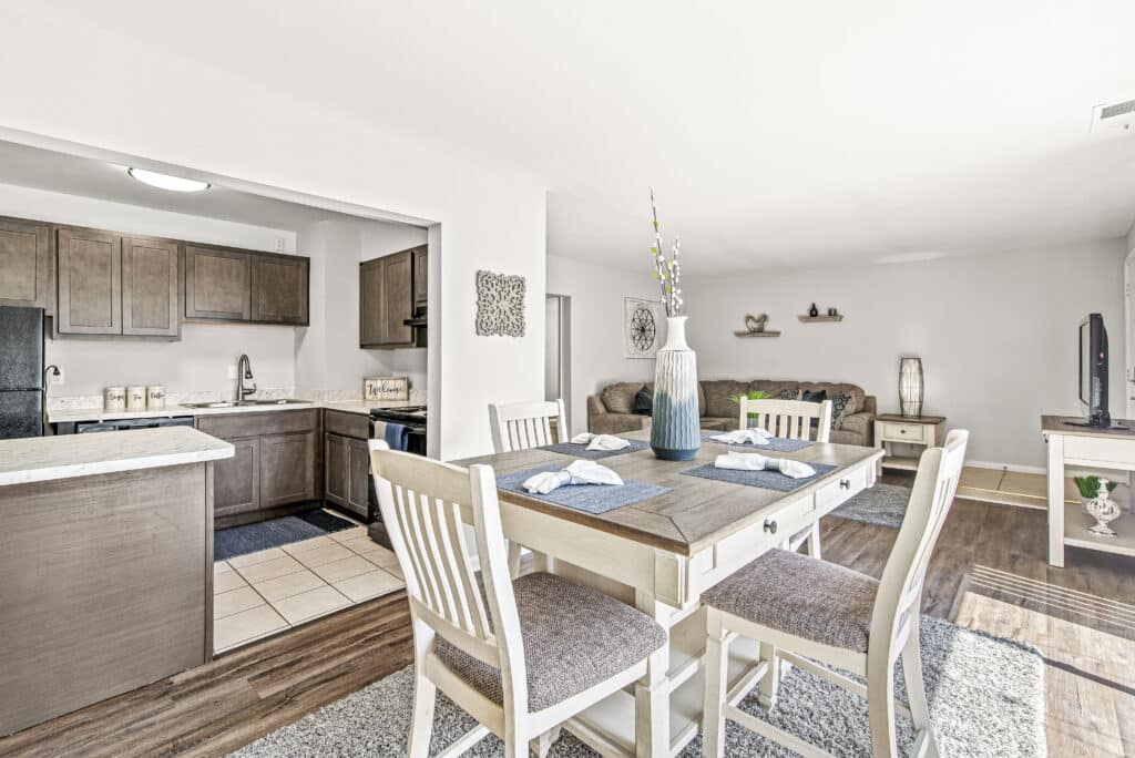 Open-concept living space featuring a dining table with four chairs, a kitchen with wooden cabinets, and a living area with a couch and TV.