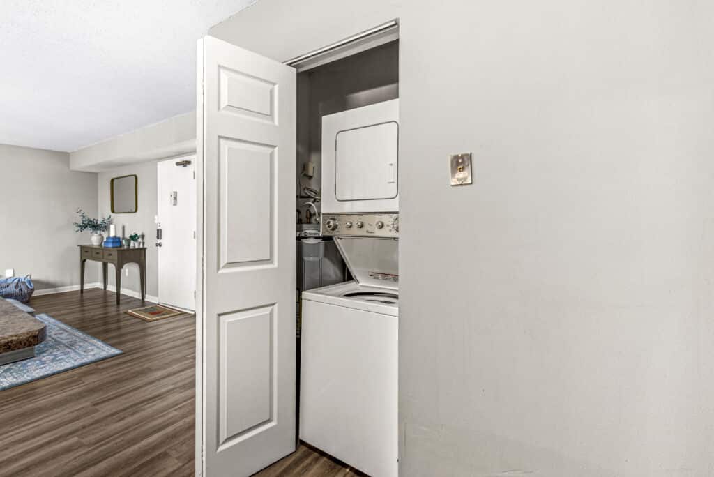 A stacked washer and dryer inside a small closet with a partially open door, located in a room with wood flooring and neutral walls.