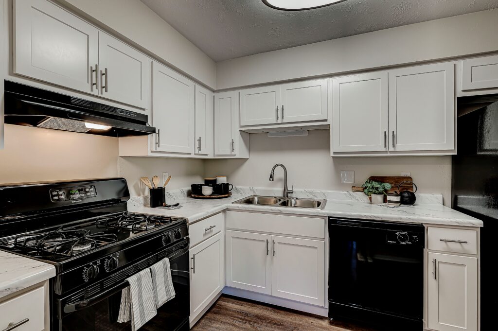 Modern kitchen with white cabinets, black appliances, a gas stove, sink, dishwasher, and marble countertop; utensils and small kitchenware are on the counters.