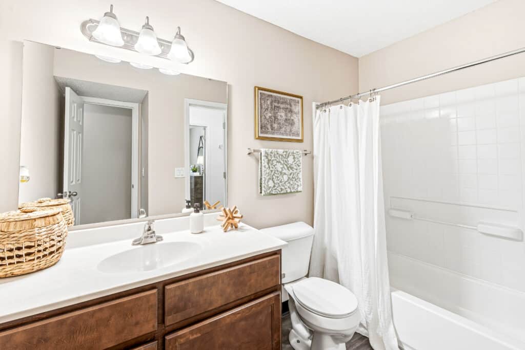 Clean bathroom with a single sink, wooden vanity, toilet, white shower curtain, and wall-mounted light fixture above a large mirror.